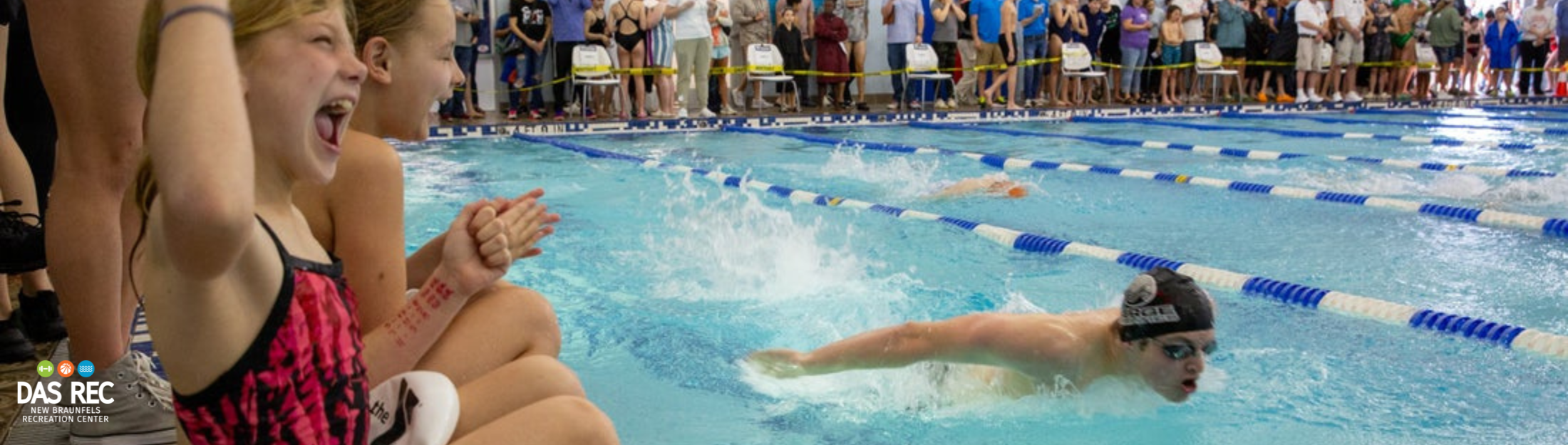 Swimmers competing during a swim meet with crowds cheering them on