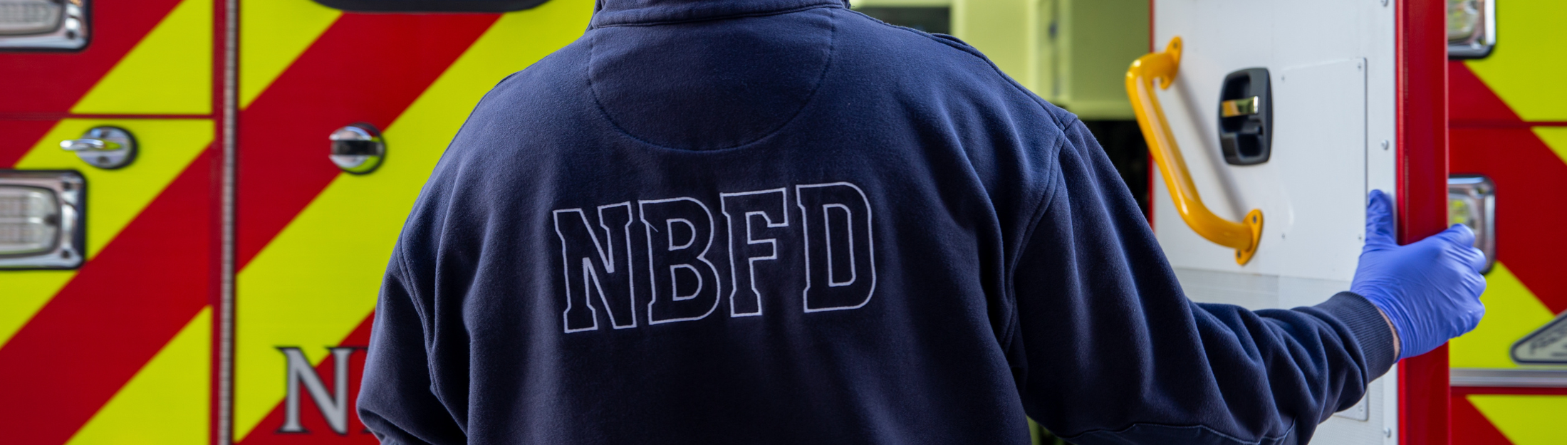 NBFD firefighter in navy uniform beside ambulance