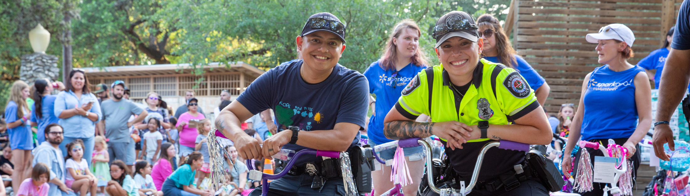 Officers smile with decorated bikes at a community event surrounded by families